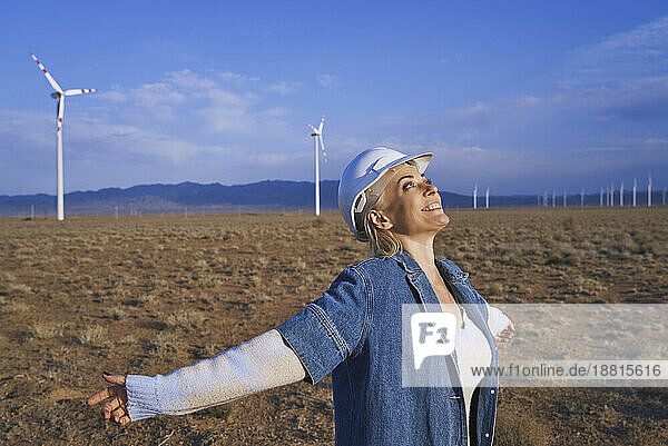 Smiling engineer looking at sky with arms outstretched standing in desert