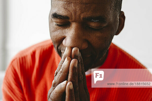 Mature man praying with hands clasped and eyes closed