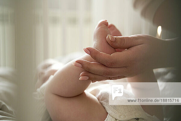 Mother holding feet of baby girl lying on bed