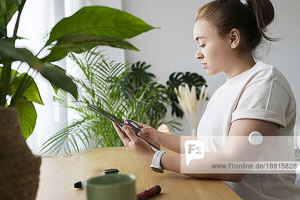 Woman with diabetes synchronizing tablet PC and glucometer on table at home