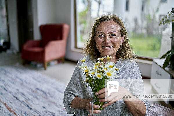 Happy senior woman with vase of flowers at home