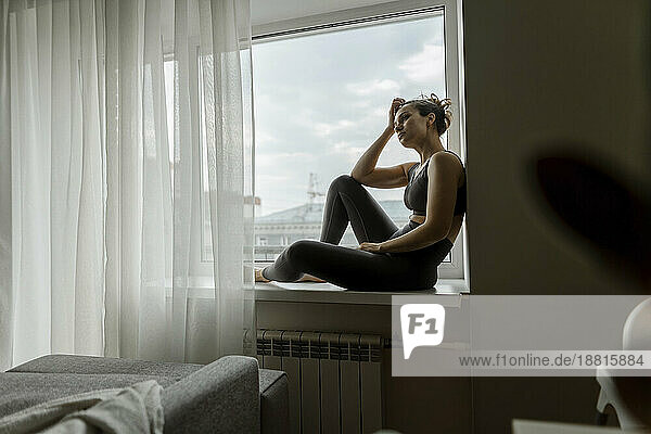 Thoughtful woman relaxing on window sill at home