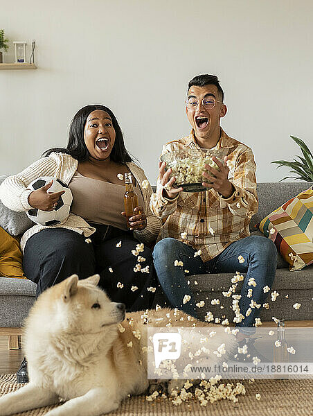 Aufgeregtes Paar feiert zu Hause mit Hund auf dem Sofa