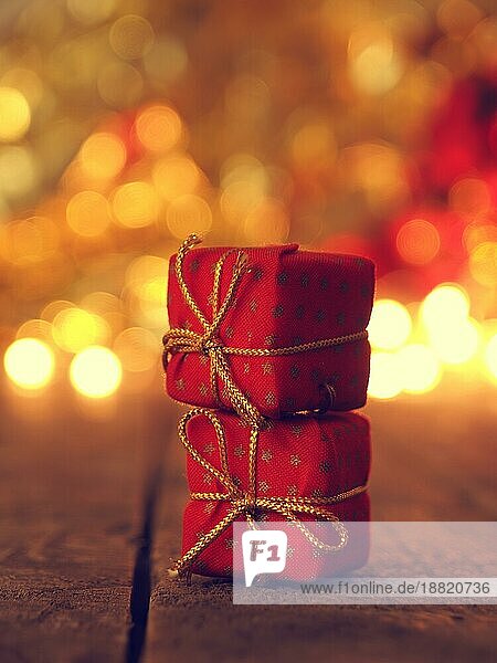 Zwei rote Weihnachtsgeschenkkartons auf einem Holztisch gestapelt  unscharfe Weihnachtsbeleuchtung im Hintergrund  selektiver Fokus im Vordergrund