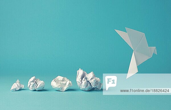 Zerknitterte Papierkugeln mit einer Origami Papiertaube  Frieden  Freiheit oder Gelegenheit Konzept auf einem blaün Hintergrund