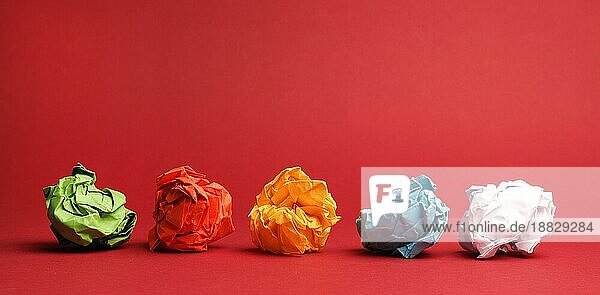 Bunte zerknüllte Papierkugeln auf rotem Studiohintergrund  Kreativität oder Diversitätskonzept  tolle Ideen  Teamarbeit