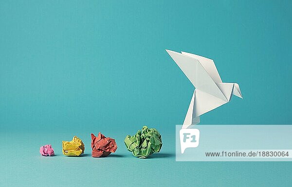 Bunte zerknitterte Papierkugeln mit einer Origami Papiertaube  Frieden  Freiheit  Vielfalt oder Gelegenheit Konzept auf einem blaün Hintergrund