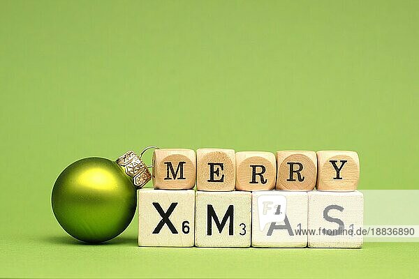 Holzklötze mit den Worten Frohe Weihnachten und einer Weihnachtskugel auf grünem Hintergrund  Platz für Text