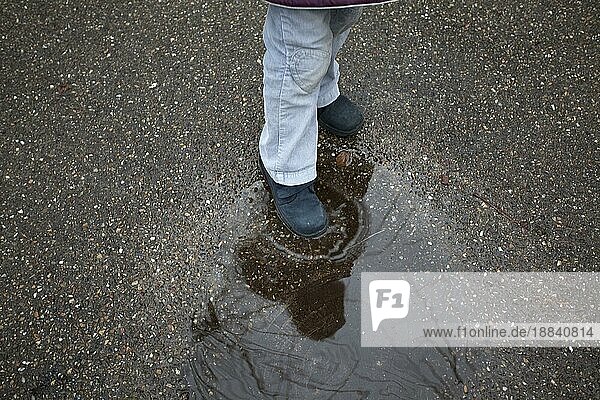 Kind  das an einem regnerischen Tag in eine Wasserpfütze tritt