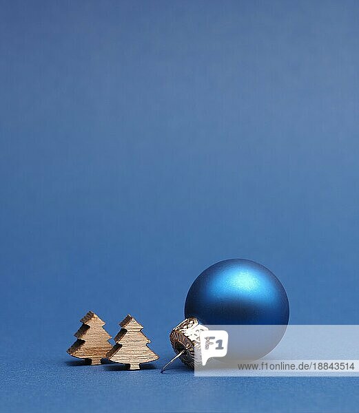 Blaue Weihnachtsbaumkugel mit kleinen hölzernen Baumformen auf einem blaün Papierhintergrund mit Platz für Ihren Text