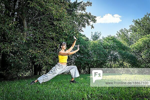 Gelassene erwachsene Frau bei einer Qigong Übung im Park. Verbindung mit der Natur und der Lebensenergie des Universums