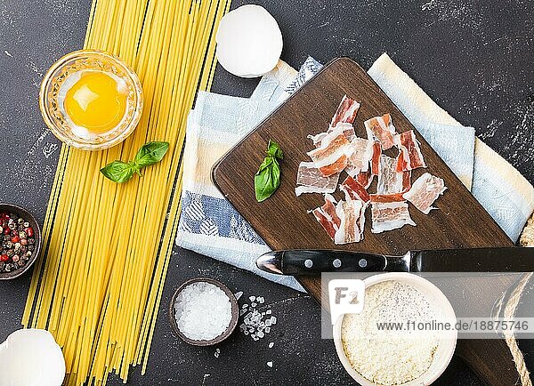 Zutaten für das Kochen traditionelle italienische Pasta Gericht Spaghetti Carbonara  rohes Eigelb  Parmesan-Käse  Speck auf Holzbrett auf schwarzem rustikalen Stein Hintergrund  Ansicht von oben. Italienisches Abendessen mit Pasta