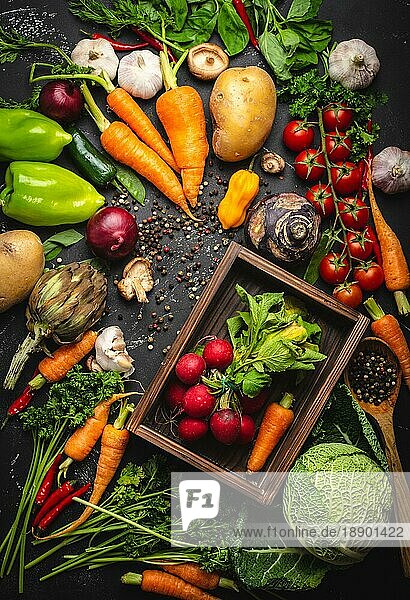 Radieschen und Karotten frische Bündel in alten Holzkiste und frischen Bauernhof Bio-Gemüse auf rustikalen schwarzen Beton Hintergrund. Herbst Ernte  vegetarische Lebensmittel oder saubere gesunde Ernährung Konzept  Ansicht von oben