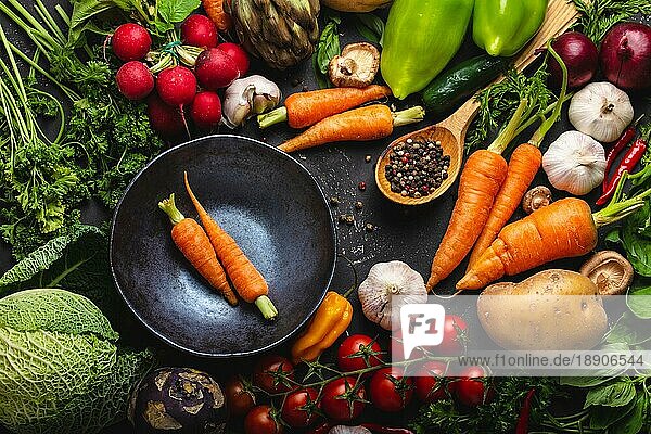 Zwei frische Bauernhof Karotten in Vintage-Schüssel und verschiedene Bio-Gemüse auf rustikalen schwarzen Beton Hintergrund. Herbst Ernte  vegetarisches Essen oder Kochen saubere gesunde Mahlzeit Konzept  Ansicht von oben