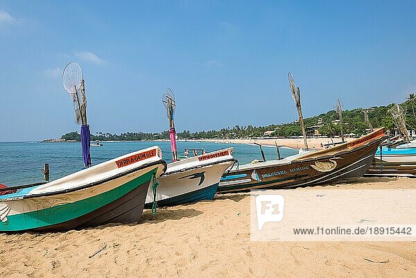 Unawatuna. Am Strand eines der wichtigsten Touristenzentren im Südwesten Sri Lankas. Touristen nehmen ein Sonnenbad und treiben Wassersport. Auslegerboote und traditionelle Fischerboote am Strand