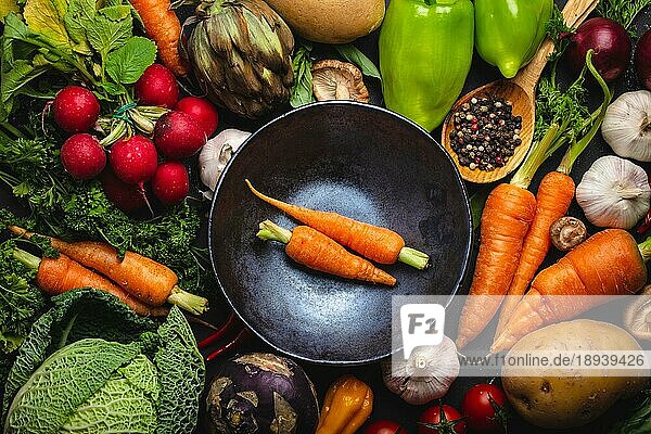 Zwei frische Bauernhof Karotten in Vintage-Schüssel und verschiedene Bio-Gemüse auf rustikalen schwarzen Beton Hintergrund. Herbst Ernte  vegetarisches Essen oder Kochen saubere gesunde Mahlzeit Konzept  Ansicht von oben