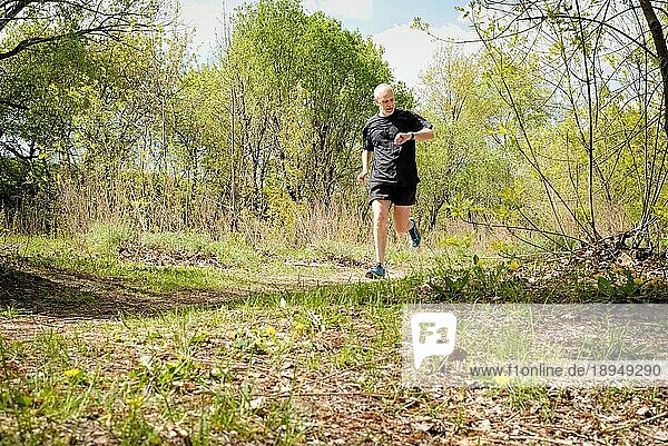Ein älterer  schwarz gekleideter Mann läuft an einem warmen Frühlingstag durch den Wald und schaut auf Zeit seiner Stoppuhr