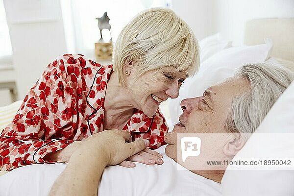 Älteres Paar liegt zusammen im Bett im Schlafzimmer und lacht sich verliebt an  Köln  Nordrhein-Westfalen  Deutschland  Europa