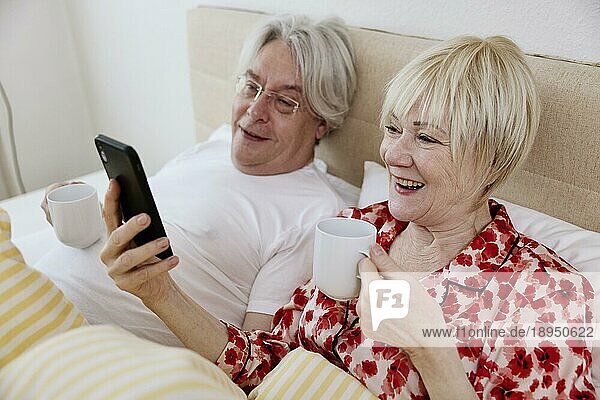 Älteres Paar liegt zusammen im Schlafzimmer im Bett und schauen zusammen auf ein Smartphone  Köln  Nordrhein-Westfalen  Deutschland  Europa