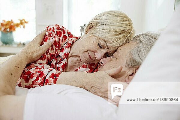 Älteres Paar  das zusammen im Bett im Schlafzimmer liegt und sich zärtlich umarmt  Köln  Nordrhein-Westfalen  Deutschland  Europa