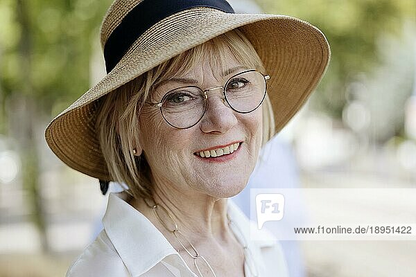 Fröhliche  lächelnde  ältere  sommerlich gekleidete Frau mit Strohhut  Brille und Perlenkette  Porträt  Köln  Nordrhein-Westfalen  Deutschland  Europa