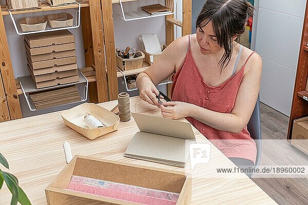 Junge Kunsthandwerkerin bindet ihre umweltfreundlichen Notizbücher in ihrer Heimwerkstatt