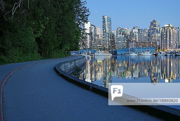 Erleuchtete Wolkenkratzer und Freizeitboote spiegeln sich im ruhigen Wasser  Teile des Sea Walls mit Radweg im Stanley Park  Abenddämmerung  Vancouver Downtown  British Columbia  Kanada  Nordamerika