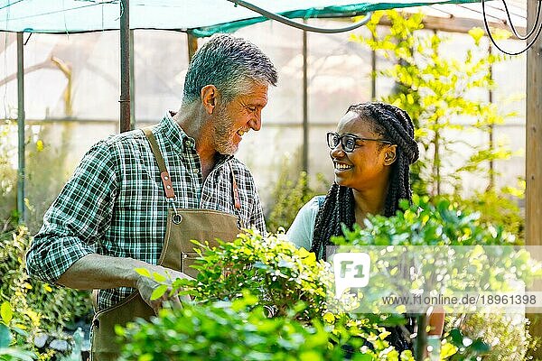 Gärtnermeister unterrichtet Schülerin in der Blumenzucht im Gewächshaus lächelnd