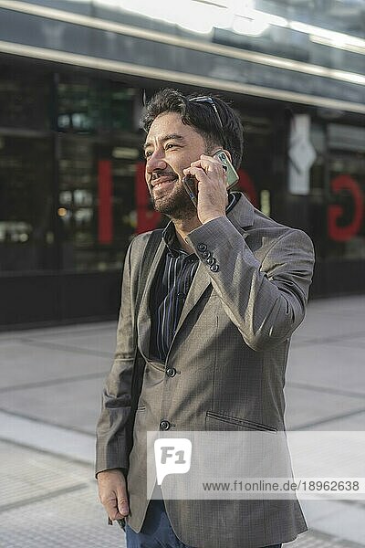 Porträt eines attraktiven lächelnden Geschäftsmannes  der vor seinem Büro mit einem Freund telefoniert