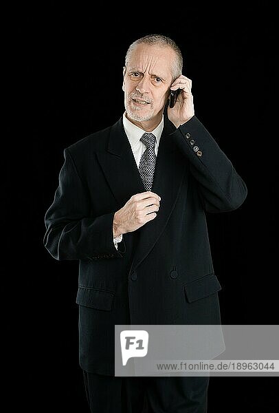 Glücklicher Geschäftsmann im schwarzen Anzug  besorgt und beschäftigt mit seinem Mobiltelefon  auf schwarzem Hintergrund