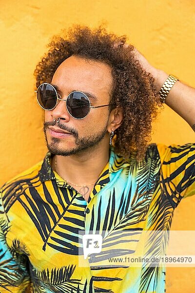 Porträt eines attraktiven Mannes mit Afrohaar im Sommer in einem Palmenhemd auf gelbem Hintergrund