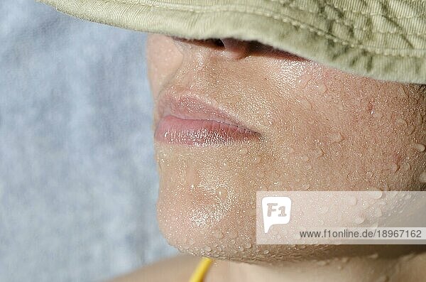 Nahaufnahme einer Frau beim Sonnenbaden mit Wassertropfen im Gesicht