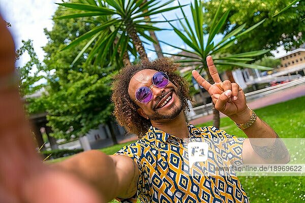 Afro haired Mann im Sommerurlaub neben einigen Palmen am Strand ein Selfie und tun den Sieg selfie. Reisen und Tourismus Konzept