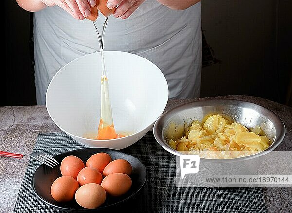 Frau  die ein Ei in eine Schüssel gießt  mit einem Teller mit Eiern und einer Schüssel mit Kartoffeln