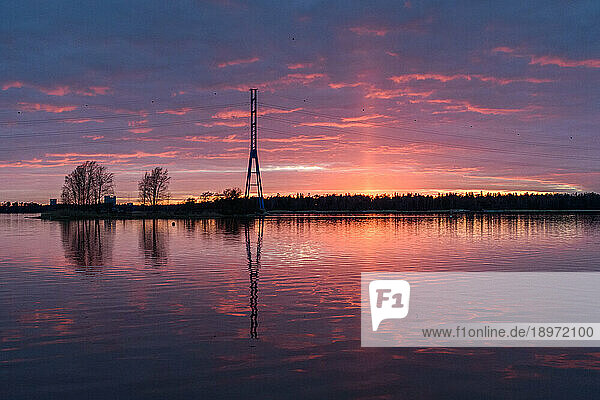 A view of a tall mast and buildings on the coastline of islands near Helsinki  at sunset.