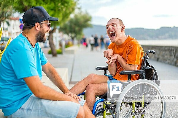 Ein behinderter Mensch im Rollstuhl mit einem Freund in den Sommerferien  der sich amüsiert und viel lacht