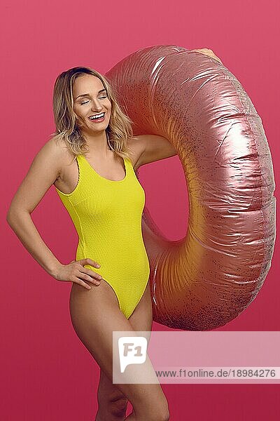 Sexy schlanke junge Frau im gelben Badeanzug  die einen großen aufblasbaren Schlauch über ihren Arm hält  während sie laut lacht
