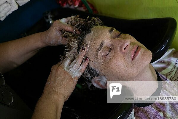 Nahaufnahme einer reifen Kundin  die sich von einem Friseur die Haare waschen lässt  nachdem sie sich im Schönheitssalon die Haare gefärbt hat. Kleine lateinische Schönheitssalon Geschäft