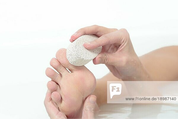 Eine Frau entspannt sich in einem heißen Seifenbad und benutzt einen Bimsstein  um ihre Füße zu peelen und abgestorbene Hautzellen von der Fußsohle zu entfernen