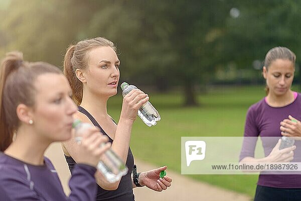 Sportliche Frauen trinken Wasser  während sie sich nach einem Outdoor Training im Park ausruhen