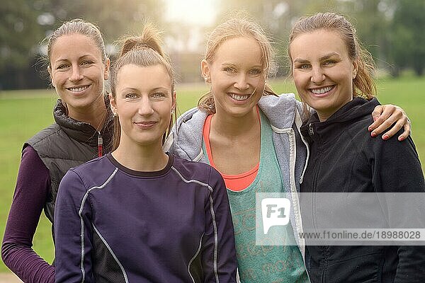 Vier glückliche  gesunde  junge Frauen in einer Reihe  die sich nach ihrer Outdoor Übung umarmen und in die Kamera lächeln