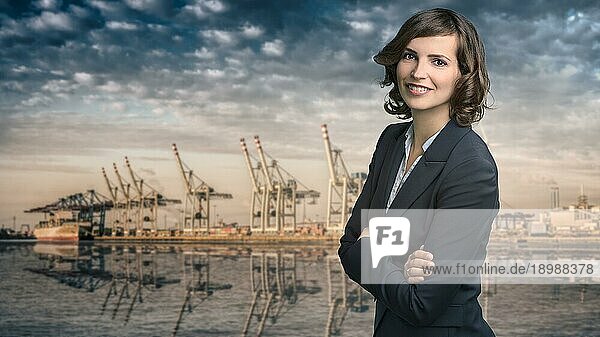 Attraktive Geschäftsfrau mit lockigen braunen Haaren  die eine elegante Jacke trägt  steht vor einem Hafen oder einem Geschäftshafen und lächelt in die Kamera  Oberkörperporträt