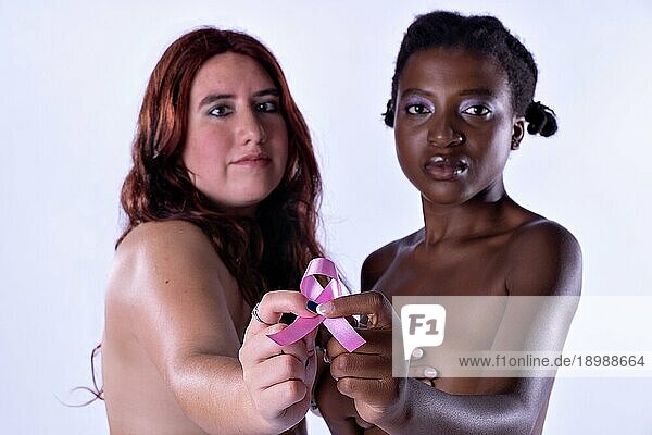 Studioporträt von zwei jungen Frauen  die ihre Brüste bedecken und in die Kamera schauen und eine rosa Schleife halten. Brustkrebs Bewusstsein Konzept. Selektiver Fokus im Symbol für Brustkrebs