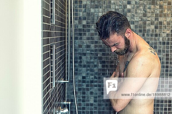 Freundlicher junger Mann mit Vollbart  der sich unter der Dusche einseift und in die Kamera lächelt  Oberkörper mit Kopierraum