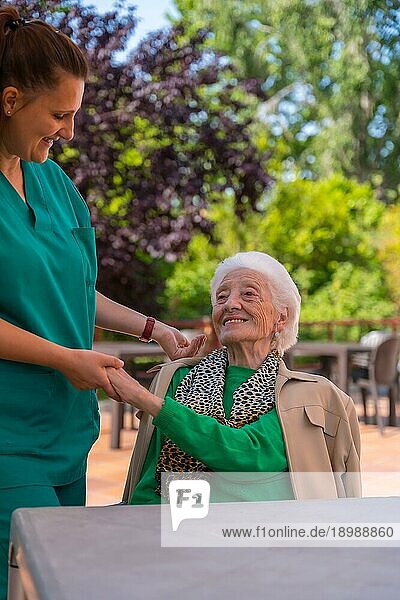 Eine ältere oder reife Frau mit einer Krankenschwester im Garten eines Pflegeheims in einem Moment der Liebe und Zuneigung
