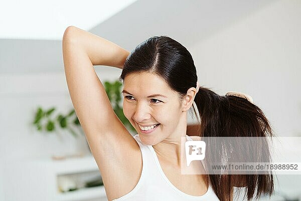 Lächelnde attraktive Frau bürstet ihr langes brünettes Haar im Badezimmer am Morgen und hält es in einer Hand in einem Pferdeschwanz  während sie mit der Bürste durch das Haar fährt