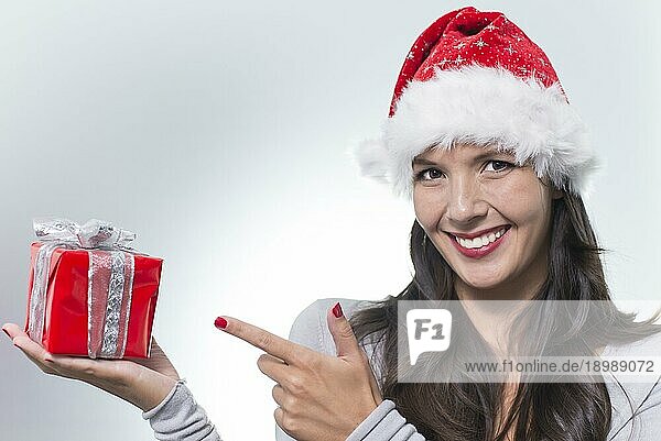 Hübsche junge Frau mit langen brünetten Haaren und einem schönen sanften Lächeln  die ein buntes rotes Geschenk für einen geliebten Menschen in der Hand hält