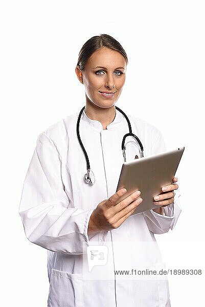 Attraktive weibliche Krankenschwester oder Ärztin in einem weißen Kittel stehend  die einen Tabletcomputer konsultiert und die Informationen mit einem freundlichen Ausdruck liest  vor weißem Hintergrund