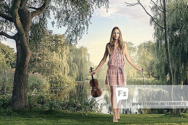 Junge Musikerin mit ihrer Geige in der Hand  die am See steht und in die Kamera schaut