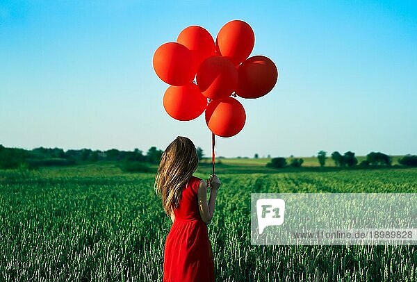 Rückenansicht der Freiheit glückliche Frau läuft mit roten Luftballons auf grünen Sommerfeld. Spaß  Glück Konzept